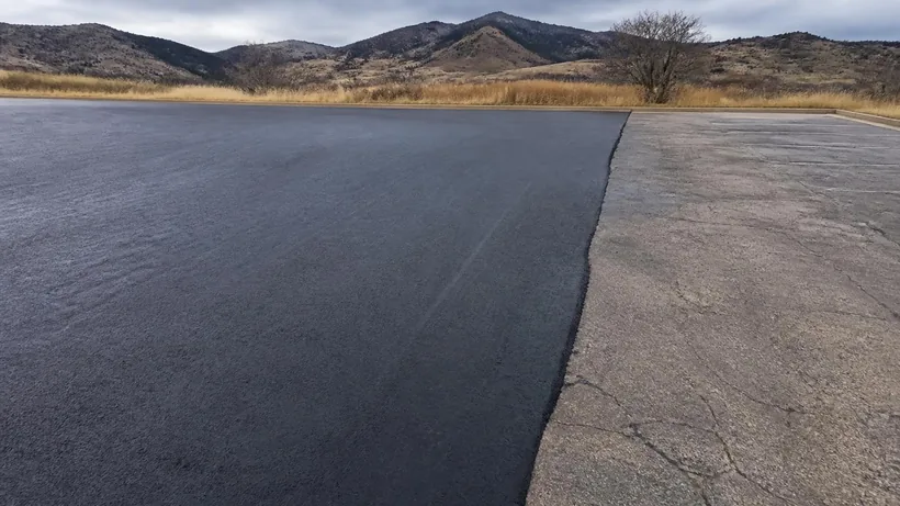 Freshly sealcoated asphalt meeting weathered, visibly cracked pavement along a straight cut edge